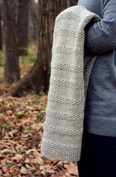 a woman standing in the woods with her back to the camera, wearing a knitted scarf