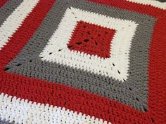 a crocheted blanket with red, grey and white squares on it's edges