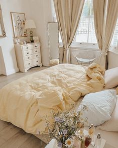 a bed sitting in a bedroom next to a window covered in yellow sheets and pillows