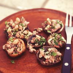 a wooden plate topped with stuffed mushrooms next to a knife and fork