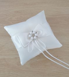 a white ring pillow with a bow on the front and beading at the back