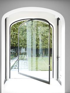 an arched glass door leading to a garden area with trees in the background and white walls