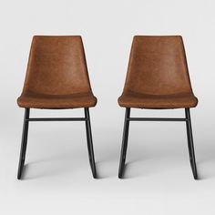 two brown leather chairs sitting next to each other on top of a white floor with black legs