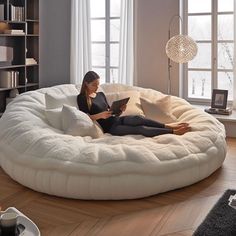 a woman laying on top of a white bean bag chair in front of a window