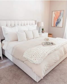 a white bed sitting in a bedroom next to a window covered in blankets and pillows