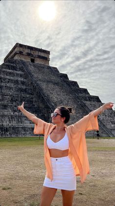 a woman standing in front of an ancient structure with her arms outstretched and eyes closed