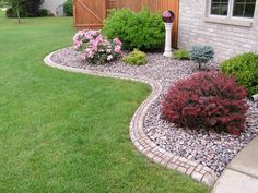 a garden with flowers and rocks in the grass next to a brick fenced yard