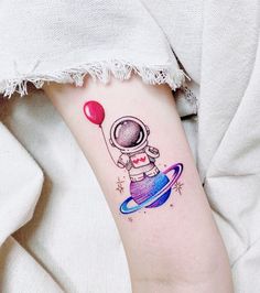 a small tattoo on the arm of a person wearing an astronaut suit and holding a red balloon