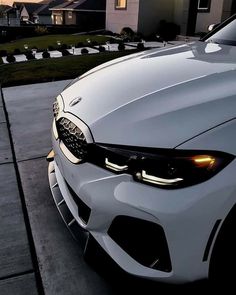 the front end of a white bmw car parked on a sidewalk next to a house