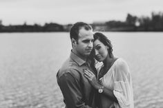 a man and woman standing next to each other near the water in black and white