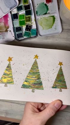 someone is painting christmas trees on paper with watercolors