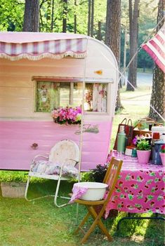 a pink trailer parked next to a picnic table with flowers on it and an american flag in the background