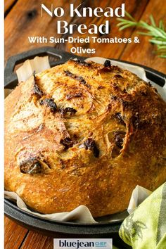 a loaf of bread sitting in a pan on top of a wooden table with the title, no knead bread with sun - dried tomatoes and olives