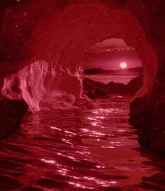 a red and black photo of water in a cave with the sun setting behind it