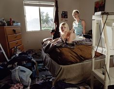 two women sitting on a bed in a messy room