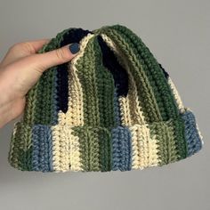 a hand holding up a crocheted green and blue beanie with stripes on it