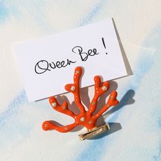 an orange coral brooch sitting on top of a piece of paper with the words queen bee