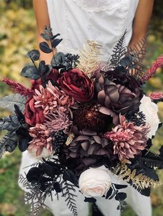 a woman holding a bouquet of flowers in her hands and wearing a white shirt with black leaves on it