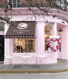 a pink store front with white tables and chairs in front of the building that has a wreath on it