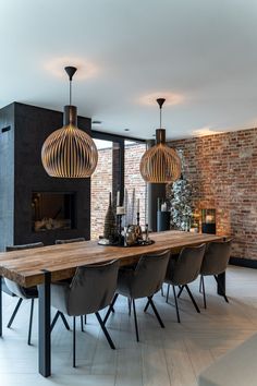 a dining room table with chairs and lights hanging from it's ceiling, in front of a brick wall