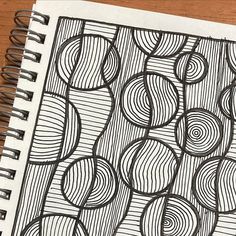 a spiral notebook with black and white designs on it, sitting on a wooden table