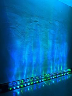 a long light fixture in front of a wall with blue and green lights on it