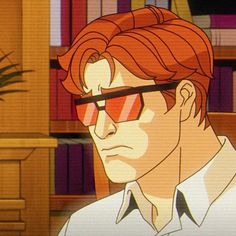 a man with red hair wearing glasses in front of bookshelves