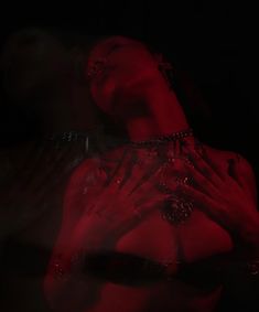 a woman with her hands on her chest in front of a dark background and red light