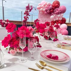 the table is set with pink and red flowers, gold place settings, and balloons