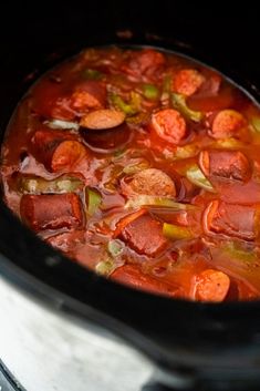 a crock pot filled with soup and hot dogs on top of the stovetop