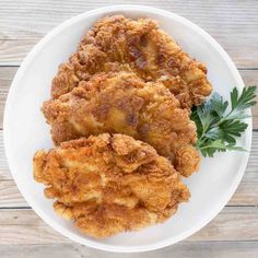 some fried food on a white plate with parsley sprigs and seasoning