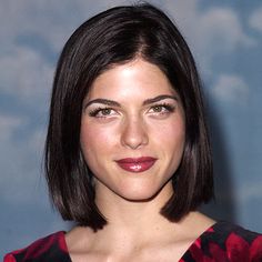 a close up of a person wearing a red and black dress with short hair, smiling at the camera