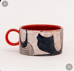 a red and black cat mug sitting on top of a white table