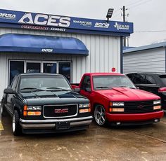 two trucks are parked in front of a car dealership with other cars outside the building