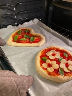 two uncooked pizzas sitting on top of an oven