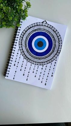 a spiral notebook with an evil eye drawn on it next to a potted plant