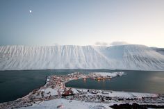 an aerial view of a snowy mountain town and lake with snow covered mountains in the background