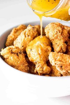 someone pouring sauce on some fried food in a white bowl