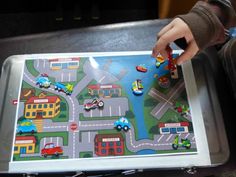 a child's hand is playing with a toy city map on a metal tray