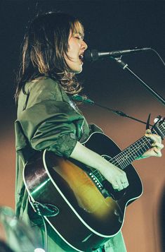 a woman singing into a microphone while holding a guitar