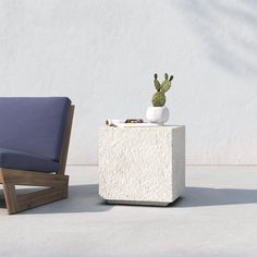 a chair next to a table with a potted cactus on it and a white wall behind it