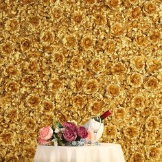 a table topped with a vase filled with flowers next to a wall covered in yellow roses