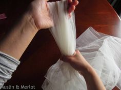 a person is holding a piece of white paper on top of a wooden table with tissue