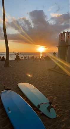 two surfboards are laying on the beach as the sun sets in the distance behind them