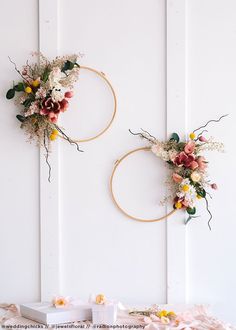 two hoop wreaths with flowers on them hanging from the side of a white wall