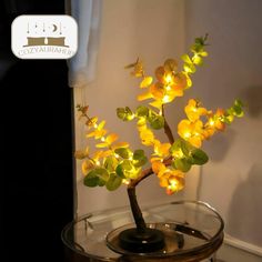 a small tree with yellow flowers in a glass vase on a table next to a window