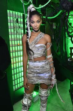 a woman standing in front of a green background wearing boots and a dress with cutouts on it