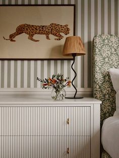 a vase with flowers sitting on top of a white dresser next to a wallpapered wall