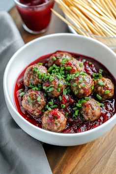 a white bowl filled with meatballs covered in cranberry sauce and garnished with green onions