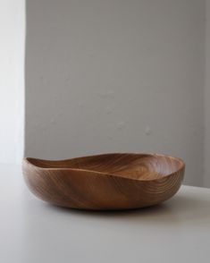 a wooden bowl sitting on top of a white table next to a wall and window